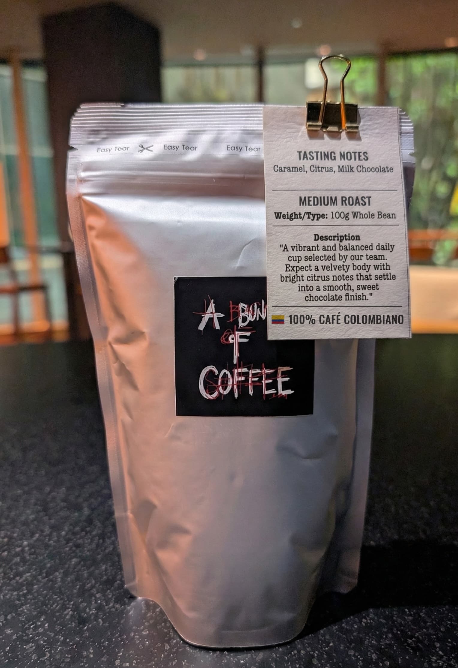 A Bunch Of Coffee 100g bag of beans with a hang tag reading 100% Café Colombiano beside a Colombian flag